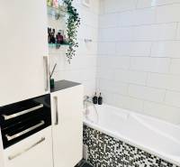 Badezimmer in einer 3-Zimmer-Wohnung mit weißer Badewanne, modernen Fliesen und Stauraum.
