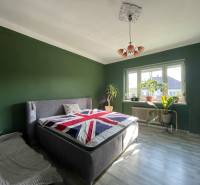 Spálňa v rodinnom dome s posteľou, zelenými stenami a podlahou s dreveným dekorom.