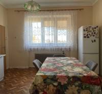 Kuchyňa v rodinnom dome s podlahou s dreveným dekorom a kvetinovým obrusom na stole.