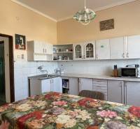 Kuchyňa v rodinnom dome s kvetinovým obrusom, bielymi skrinkami a farebnými stenami.