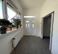 Chodba v rodinnom dome s bielymi stenami, podlahou s dreveným dekorom a izbovými rastlinami.