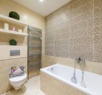 Badezimmer mit Dusche, Badewanne und Regalen in einer 2-Zimmer-Wohnung mit neutralen Fliesen.