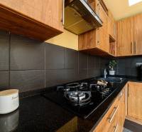 Küche mit Gasherd, dunklen Fliesen und Holzschränken in einer 2-Zimmer-Wohnung.