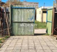 Der Hof bei der Hütte in Poltár mit einem Tor und Betonpflaster unter blauem Himmel.