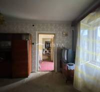 Ein Zimmer in einem Einfamilienhaus mit Retro-Möbeln, einem alten Fernseher, einem Fenster mit Blumen-Vorhängen.