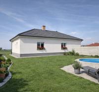 Ein Einfamilienhaus in Zemianska Olča mit Rasen, Pool und Blumenbepflanzung auf dem Grundstück.