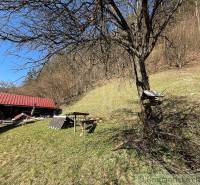 Eine Hütte bei Moštenica, umgeben von Bäumen und grasbewachsenen Hügeln bei sonnigem Wetter.