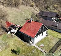 Eine Hütte in Moštenica mit einem schrägen roten Dach, umgeben von Grün und hügeligem Gelände.