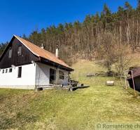 Eine Hütte in Moštenica, umgeben von einer Wiese und einem Wald im Hintergrund.