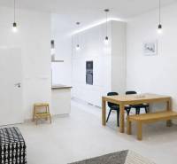 Innenraum einer 2-Zimmer-Wohnung mit weißen Wänden, einem Holztisch und einem schwarzen Sofa.