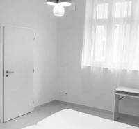 Weißes Zimmer mit Doppelbett, Tisch und Hängelampe in einer Zweizimmerwohnung.