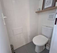 Toilette mit weißen Fliesen und dekorativem Regal in Geschäftsräumen.