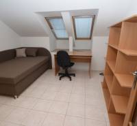 Ein Zimmer in einem Einfamilienhaus mit Bett, Tisch, Regalen, Fliesenboden und Dachfenstern.