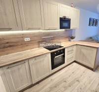 Küche mit Holzboden in einer 2-Zimmer-Wohnung, helle Holzschränke und eingebaute Geräte.