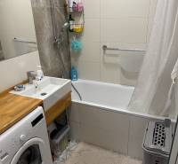 Badezimmer mit Duschwanne und Waschmaschine in einer 4-Zimmer-Wohnung mit eleganten Fliesen.
