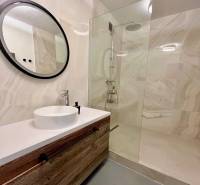 Badezimmer mit einem Holzschrank, einem runden Spiegel und einer Duschkabine in einer 3-Zimmer-Wohnung.