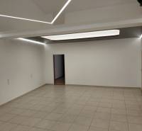 Gewerbeflächen mit weißen Wänden und Fliesenboden, Decke mit Streifenbeleuchtung.