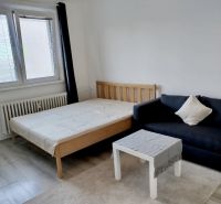 Izba s posteľou, čiernou pohovkou a stolíkom, podlaha s dreveným dekorom.
