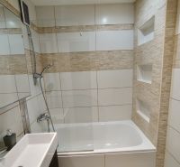Badezimmer in einer Einzimmerwohnung mit Badewanne und Duschkopf, gefliest.
