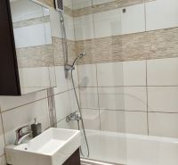 Badezimmer in einer Einzimmerwohnung mit Badewanne, Waschbecken und Fliesen in Beigetönen.