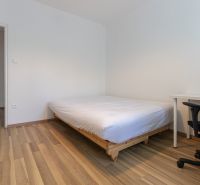 Ein Schlafzimmer in einer 3-Zimmer-Wohnung mit einem Bett, einem Schreibtisch und einem Boden in Holzoptik.