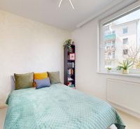 Helles Zimmer mit Bett, Regal und großem Fenster in einer Einzimmerwohnung.