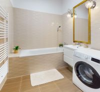 Badezimmer mit Badewanne, Waschmaschine, weißem Heizkörper, Boden mit Holzdekor und Spiegel.