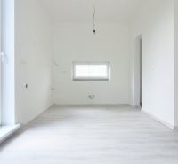 Ein Zimmer in einem Einfamilienhaus mit weißen Wänden und einem Boden in Holzoptik.