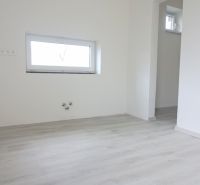 Ein Zimmer in einem Einfamilienhaus mit einem Holzboden und einem kleinen Fenster.
