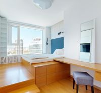 Helles Schlafzimmer mit hohem Fenster, Schreibtisch und Holzboden.