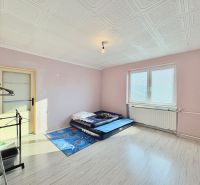 Ein Zimmer in einem Einfamilienhaus mit einer Matratze auf dem Boden, hellrosa Wände und ein großes Fenster.