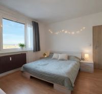 Schlafzimmer in einer 4-Zimmer-Wohnung mit Bett, Vorhängen und Boden in Holzoptik.
