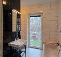 Badezimmer mit Badewanne und Waschbecken in einem Einfamilienhaus, weiße und schwarze Fliesen, Fenster mit Aussicht.