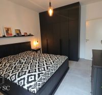 Schlafzimmer mit schwarzen Möbeln, künstlerischen Dekorationen und gemustertem Bettüberwurf.