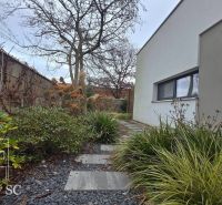 Ein Einfamilienhaus in Senec mit einem gepflegten Gartenweg, verziert mit Kieselsteinen und grünen Pflanzen.