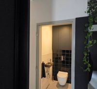 Toilette im Einfamilienhaus mit schwarzen Fliesen und hellem Boden.