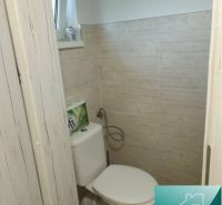 Toilette in einer Hütte mit Holzboden und beigefarbenen Fliesen.