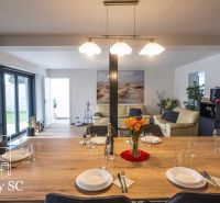 Esstisch mit Gläsern und Tellern in einem Einfamilienhaus, im Hintergrund das Wohnzimmer.