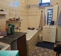 Badezimmer in einem Einfamilienhaus mit Badewanne, Waschbecken und Aufbewahrungsschränken. Geflieste Wände.