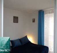 Schlafzimmer in einer Einzimmerwohnung mit blauen Vorhängen und einfacher Dekoration.