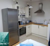 Küche in einer Einzimmerwohnung mit weißen Schränken, einem Kühlschrank aus Edelstahl und einem Herd.