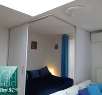 Schlafzimmer in einer Einzimmerwohnung mit blauen Vorhängen und Bildern an der Wand.