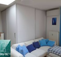 Helles Wohnzimmer in einer Einzimmerwohnung mit weißem Sofa und blauen Kissen.