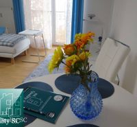 Ein Zimmer in einer Einzimmerwohnung mit einem Tisch, Blumen und einem Boden in Holzoptik.