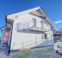 Ein Einfamilienhaus in Hrnčiarovce nad Parnou mit weißer Fassade und einem Balkon auf einem Kieshof.