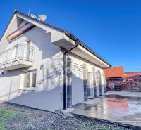 Ein Einfamilienhaus in Hrnčiarovce nad Parnou mit einer Betonterrasse und einem Balkon im Obergeschoss.