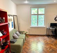Ein Zimmer in einer 2-Zimmer-Wohnung mit einem Boden in Holzoptik, einem Sofa, einem Schreibtisch und einem roten Regal.
