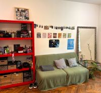 Wohnzimmer in einer 2-Zimmer-Wohnung mit rotem Regal und Holzboden.
