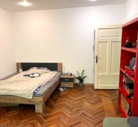 Schlafzimmer mit Bett, rotem Regal und Holzboden in einer Zweizimmerwohnung.