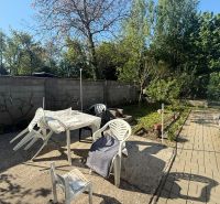 Der Garten des Ferienhauses in Sekule mit Plastikmöbeln und Bäumen am Rand.